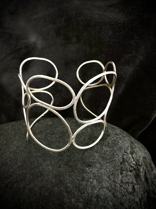 One-of-a-kind sculptural sterling silver cuff bangle with textured overlapping loops, on dark stone