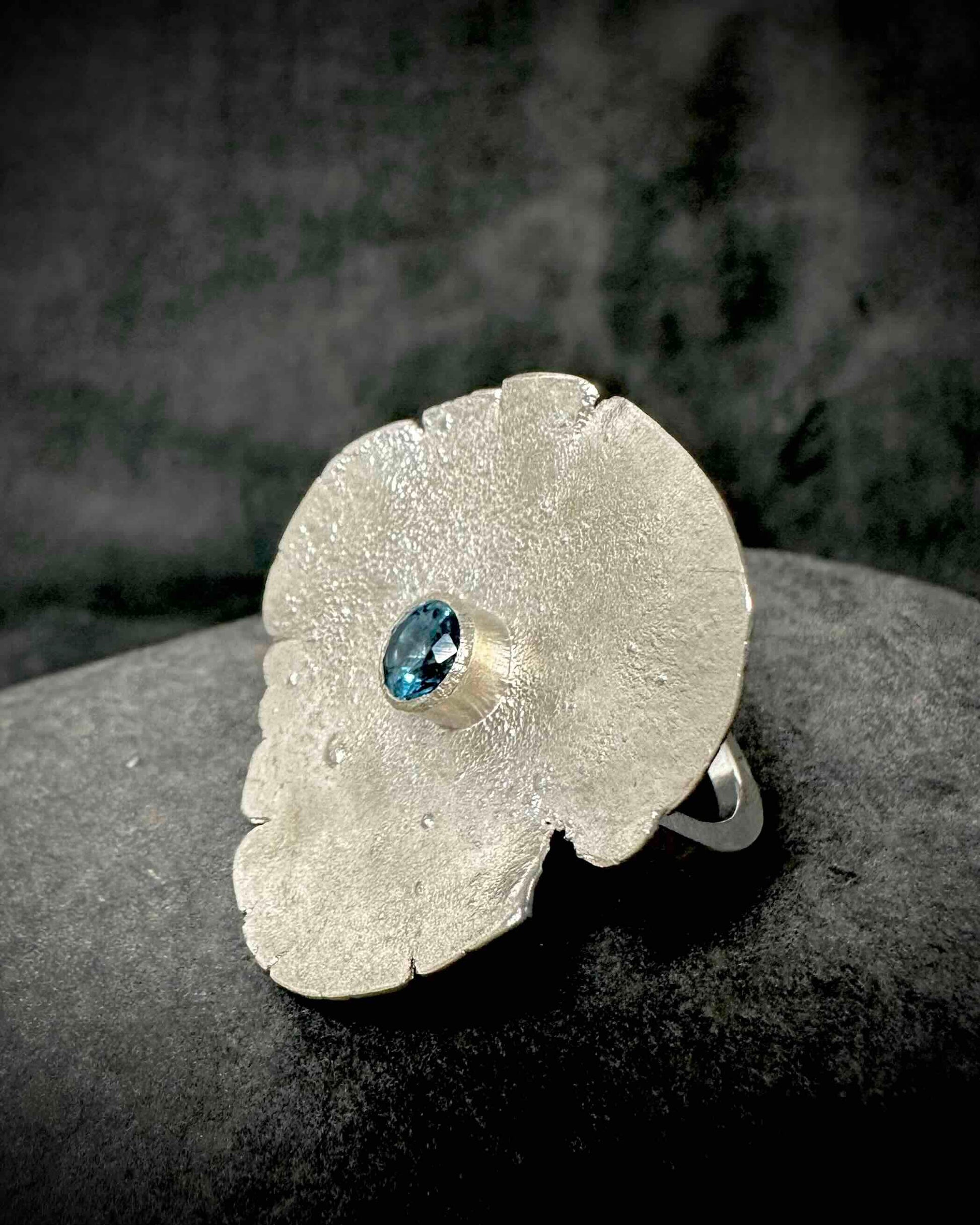 Side view of sculptural sterling silver ring showing textured band and bezel-set blue topaz