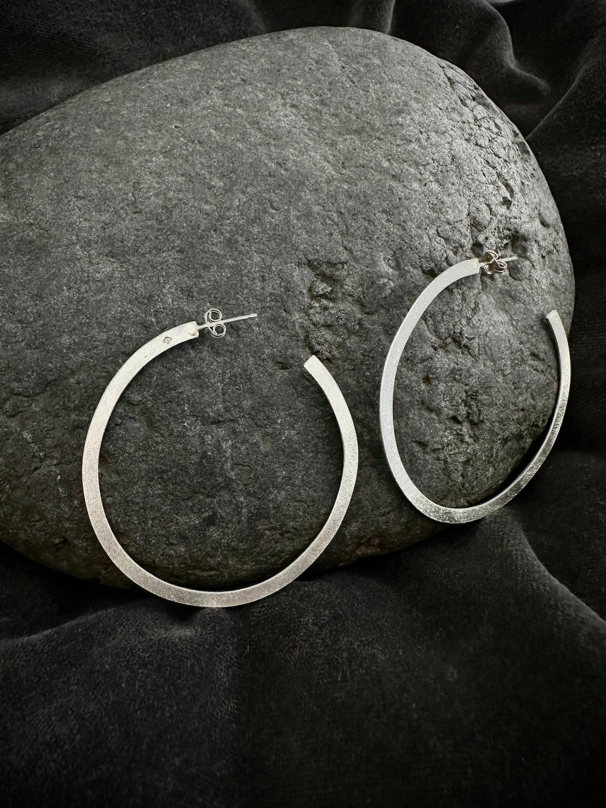 Sterling silver hoop earrings resting on dark stone - large round hoops