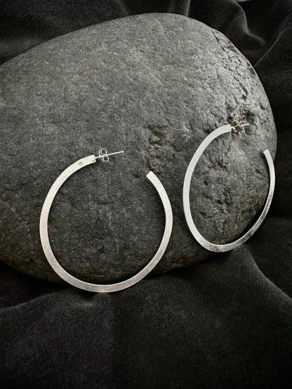 Sterling silver hoop earrings resting on dark stone - large round hoops
