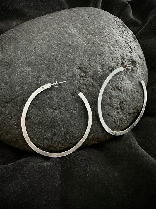Sterling silver hoop earrings resting on dark stone - large round hoops