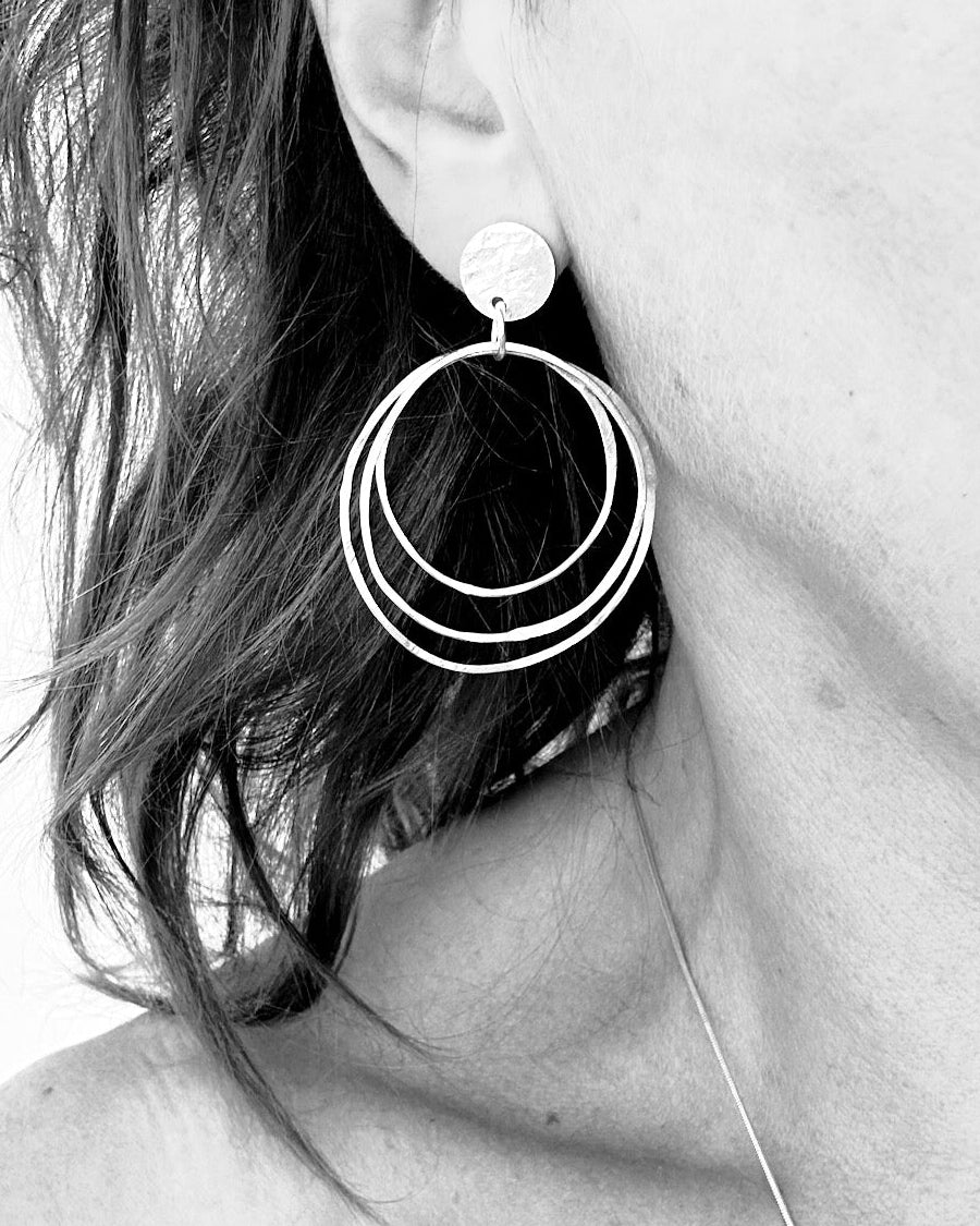 A close-up black and white photograph of a person's ear wearing a large, multi-ring hoop earring.