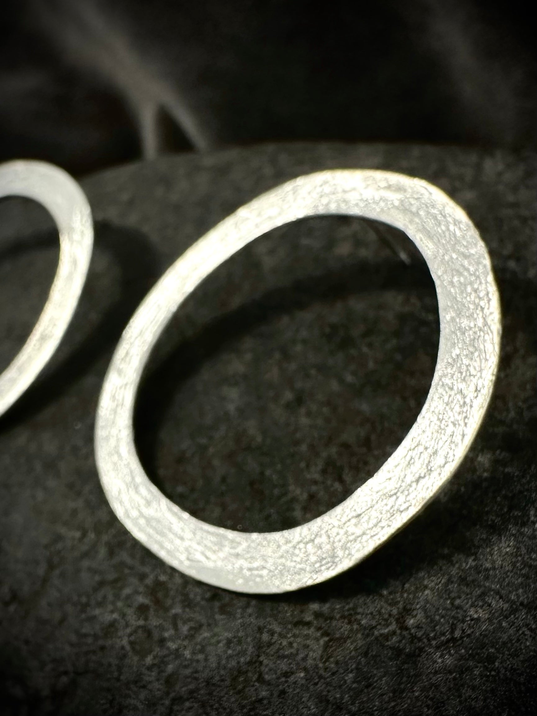 Close-up of hand-hammered sterling silver circle hoop earring with textured finish, resting on dark stone