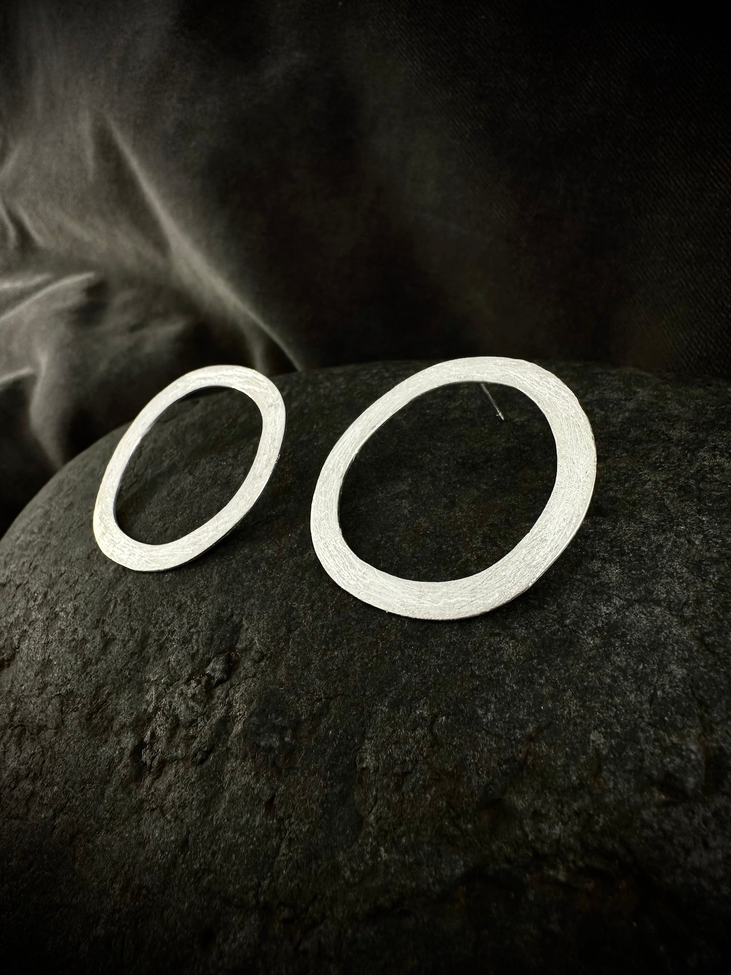 Pair of hand-hammered sterling silver circle hoop earrings with organic textured finish on dark stone