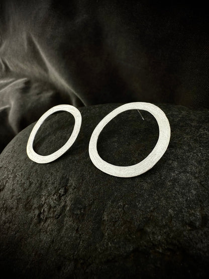 Pair of hand-hammered sterling silver circle hoop earrings with organic textured finish on dark stone