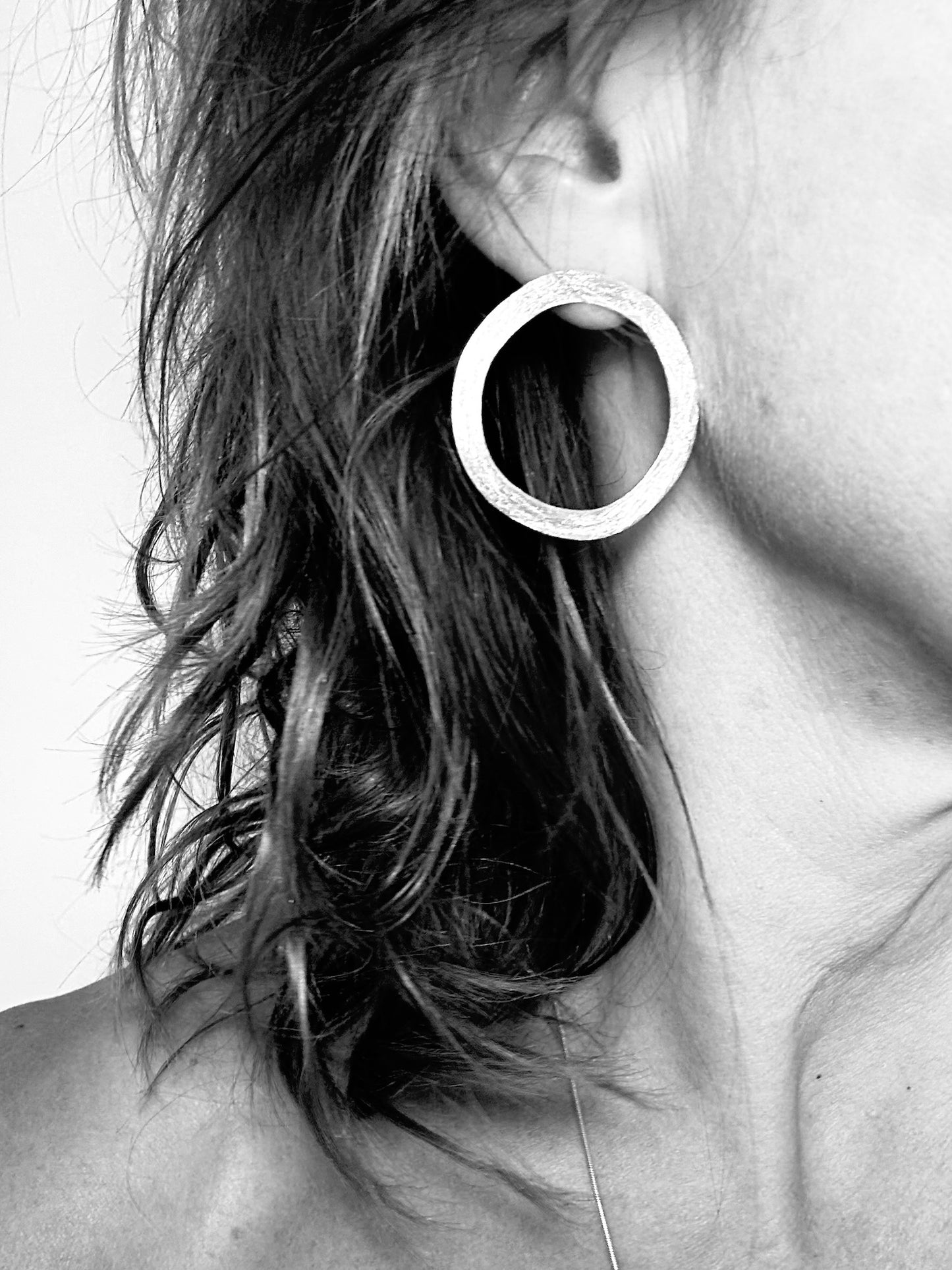 Woman wearing textured sterling silver circle hoop earring, black and white styled photo